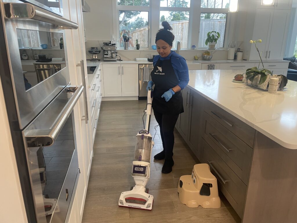 A Rain City Maids cleaner vacuuming a kitchen floor