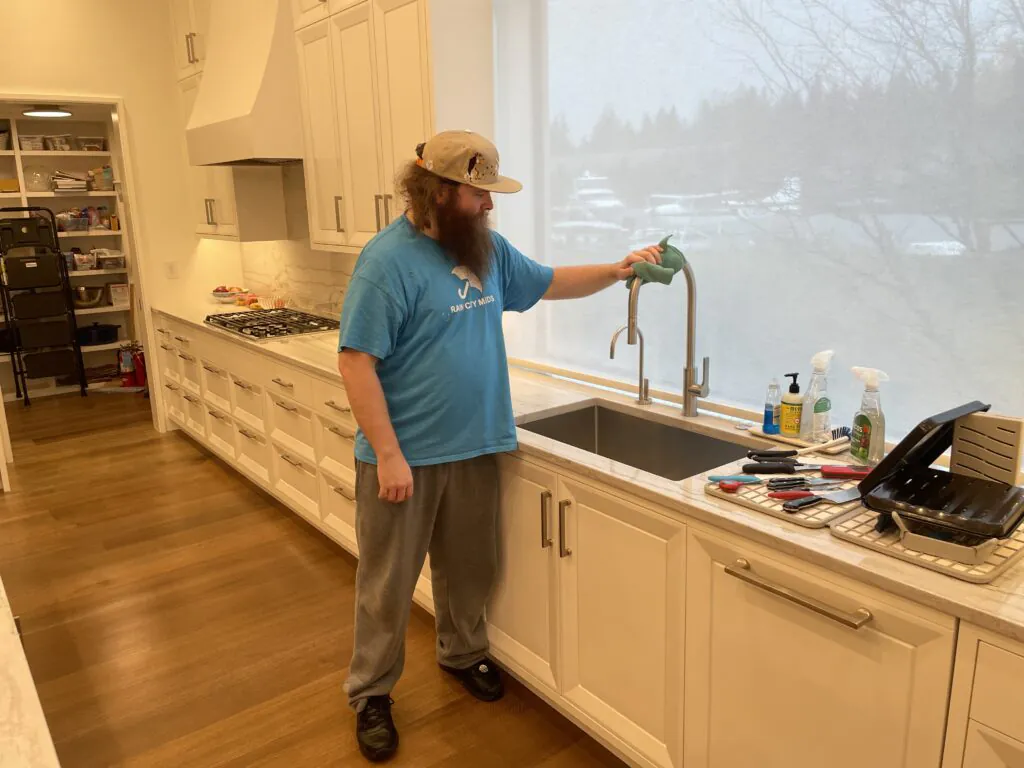 A Rain City Maids cleaner cleaning a kitchen sink and countertop