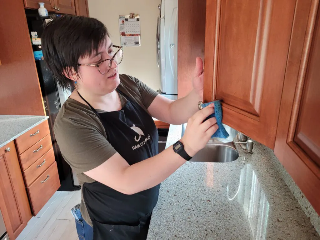 A Rain City Maids cleaner wiping down kitchen cabinets and countertops