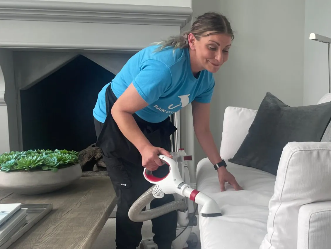 A Rain City Maids house cleaner detailing a sofa in a living room