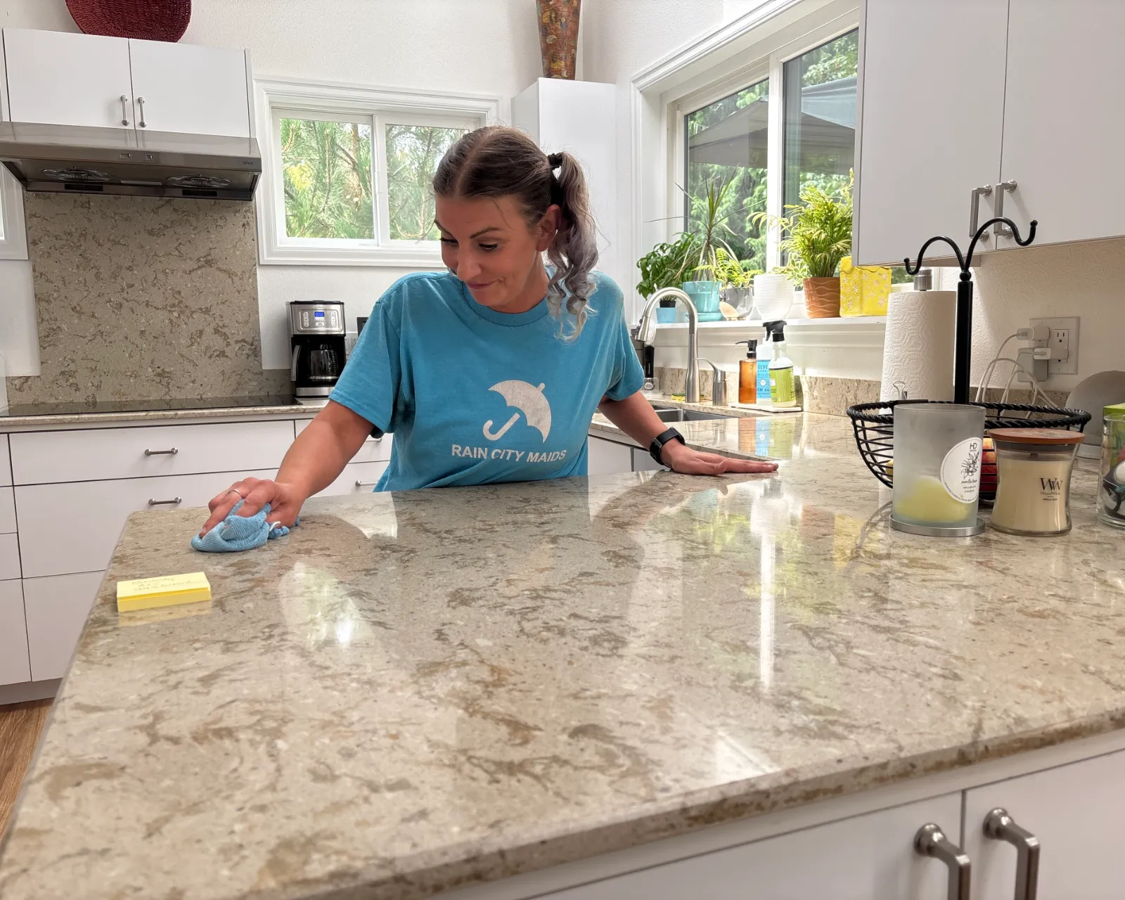 A Rain City Maids cleaner wiping down a granite kitchen counter