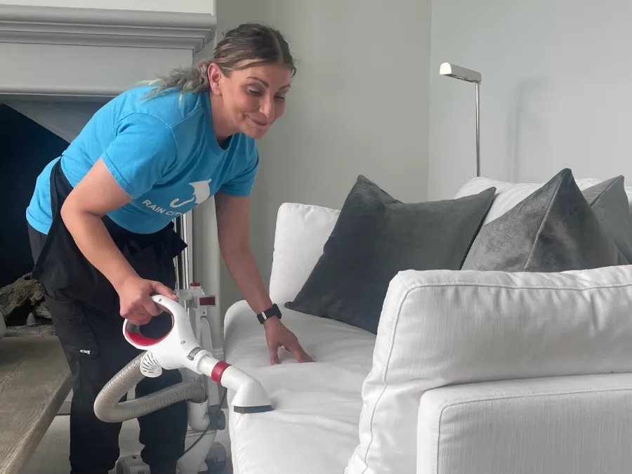 A Rain City Maids cleaner vacuuming a white sofa