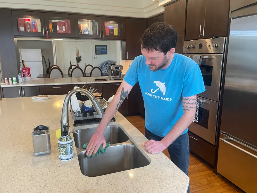 A Rain City Maids cleaner cleaning a kitchen sink